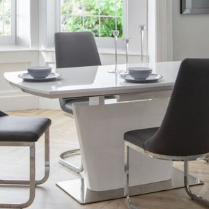 COMO High Gloss White Extendable Dining Table with butterfly extension system, paired with six black quilted chairs in a modern dining room setting.